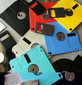 This image shows a pile of partially disassembled colorful floppy discs haphazardly arranged, overlapping one another, on a light-grey carpet. 